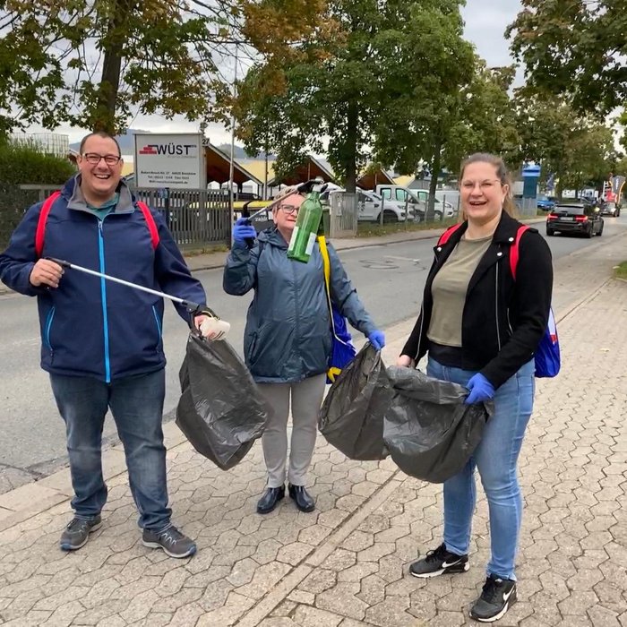 Three volunteers wearing backpacks and gloves participate in a community cleanup