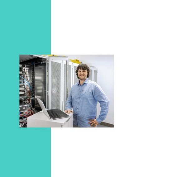 A man in a light blue shirt stands in a server room