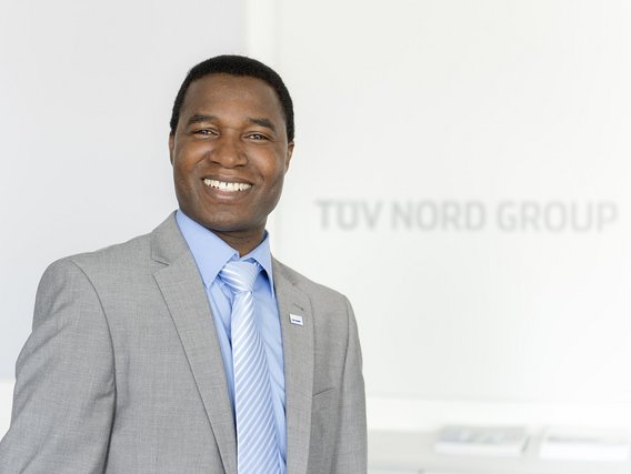 Portrait of a colleague in front of a TÜV NORD GROUP Logo