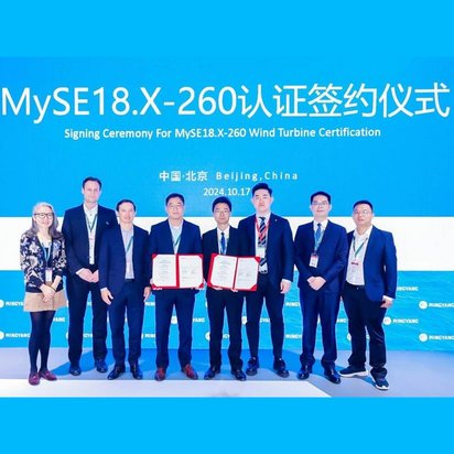Eine Gruppe von neun Personen steht auf einer Bühne vor einem großen blauen Hintergrund mit weißer Schrift. Der Text auf der Leinwand zeigt die Worte „Signing Ceremony For MySE18.X-260 Wind Turbine Certification“ und den Veranstaltungsort „Beijing, China“ mit dem Datum „2024.10.17“. Zwei Personen in der Mitte halten feierlich geöffnete Zertifikatsmappen in die Kamera. Die Anwesenden tragen formelle Kleidung mit Namensschildern und sehen professionell aus. Die Veranstaltung ist Teil einer Zertifizierungszeremonie für eine Windkraftanlage.