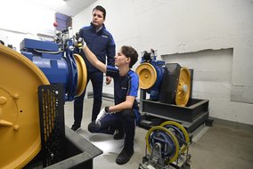 Kay Justus Kornatzki (front) and Michael Gostav Joran Gandolfo from TÜV NORD are carrying out inspections in the machine room of a lift system
