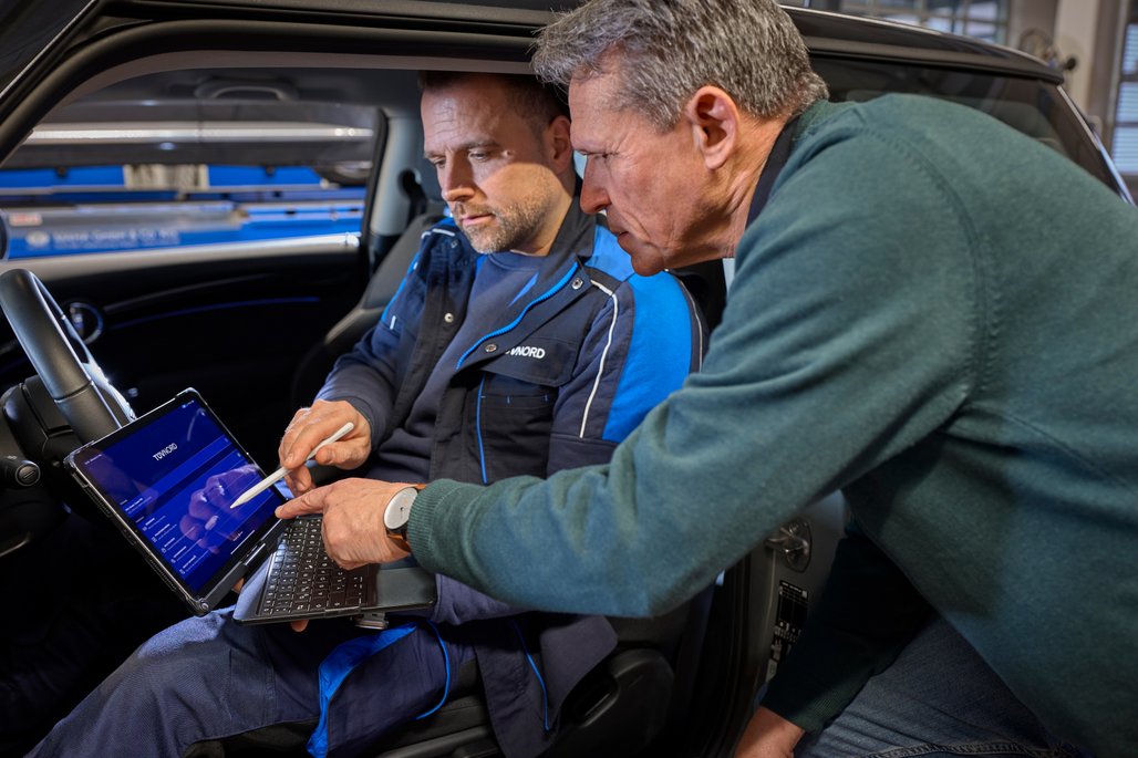 Zwei Personen im Auto, eine nutzt ein Tablet zur Fahrzeugdiagnose. Moderne Technologie in der Automobilwartung.