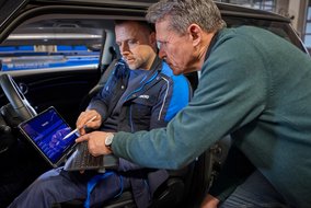 Zwei Personen im Auto, eine nutzt ein Tablet zur Fahrzeugdiagnose. Moderne Technologie in der Automobilwartung.