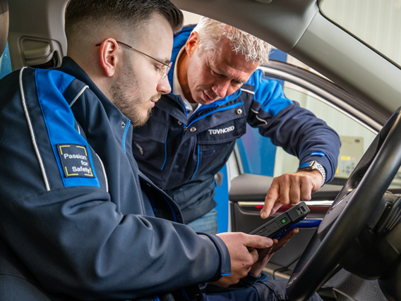 Zwei TÜV NORD Mitarbeiter arbeiten im Innenraum eines Autos mit einem Diagnosegerät.