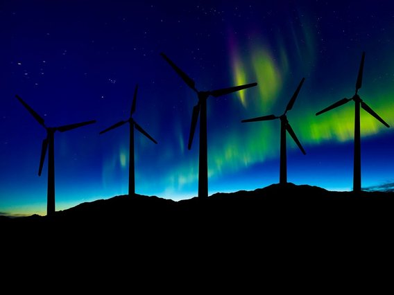 Wind turbines on a hill against a night sky illuminated.