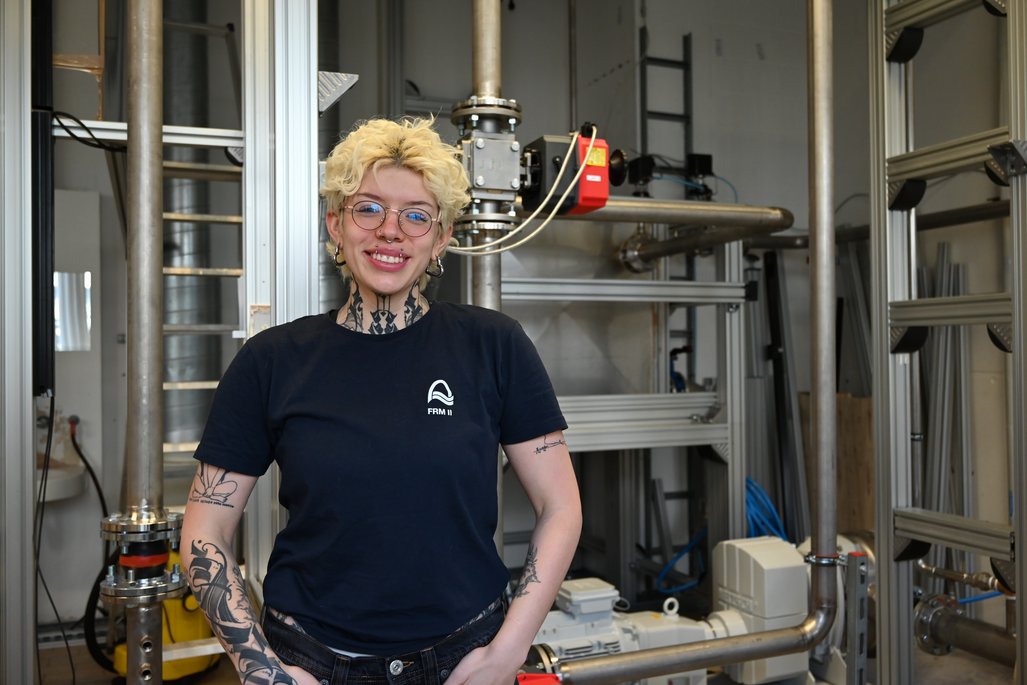 Liliana Quintero Zambrano lächelt in einem dunklen T-Shirt mit Logo vor einer technischen Anlage.