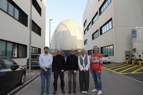 Fünf Personen posieren vor modernen Institutsgebäuden und der markanten Atom-Ei-Kuppel in Garching.