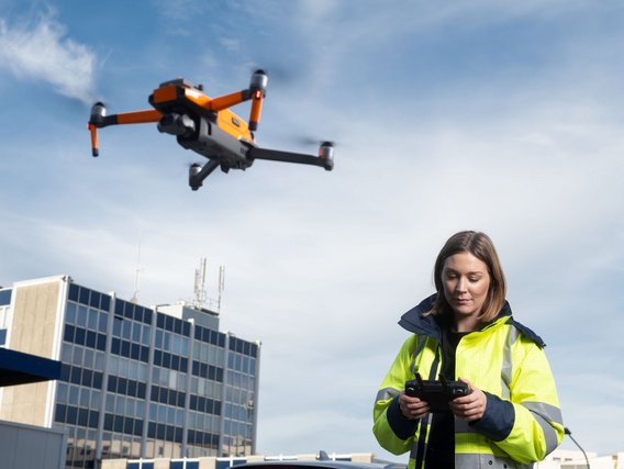 A woman in a high-visibility jacket operates a drone with a remote controller