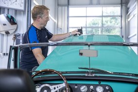 Prüfer von TÜV NORD bei der Inspektion eines Oldtimers in der Werkstatt, mit einem Messgerät zur Überprüfung der Fahrzeugoberfläche.