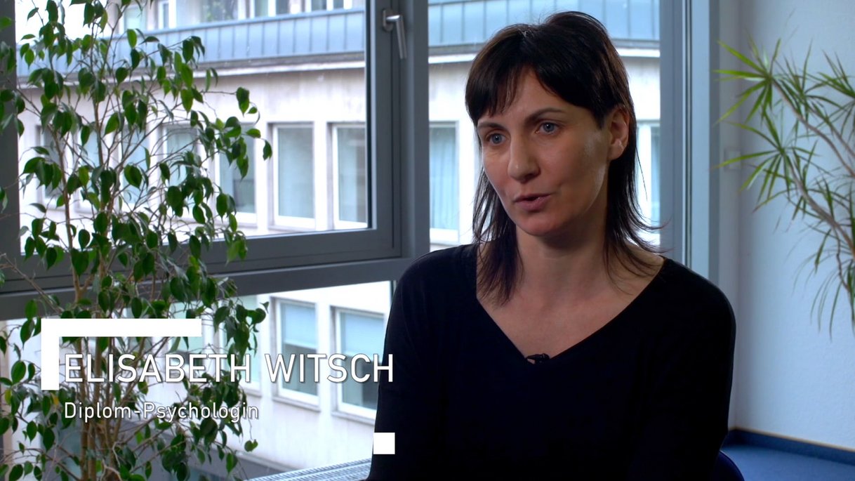 Das Bild vermittelt einen professionellen und nahbaren Eindruck von Elisabeth Witsch. Sie sitzt in einem modern eingerichteten Raum mit großen Fenstern und Pflanzen. Als Diplom-Psychologin ist sie Teil eines Mitarbeiter-Testimonials der TÜV NORD GROUP.