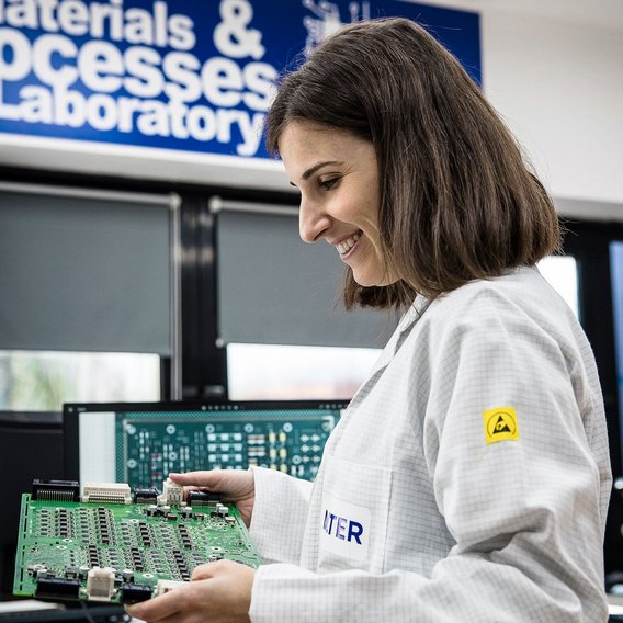 A female engineer in an anti-static lab coat inspects a circuit board